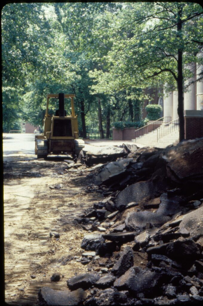 A color photo of the asphalt from Campus Drive piled up on the right with a backhoe in the background in front of Trinkle Library (Now James Farmer Hall). 