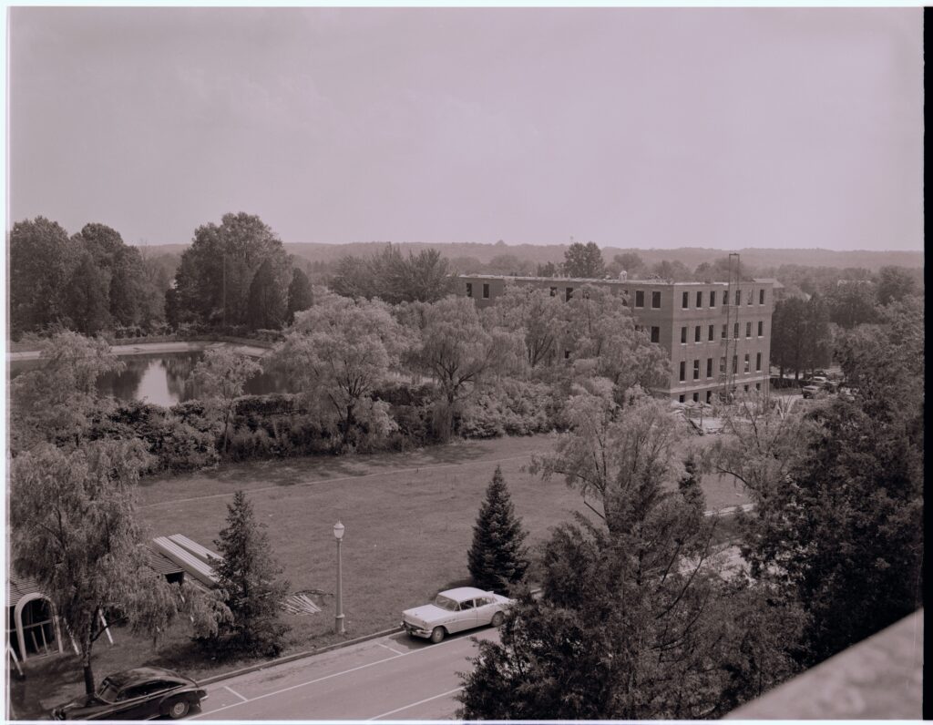 A black and white photo overlooking Double Drive and the city reservoir what is now Jefferson Square. Combs hall is on the right and still under construction in this photo without a roof and with empty spaces for windows.